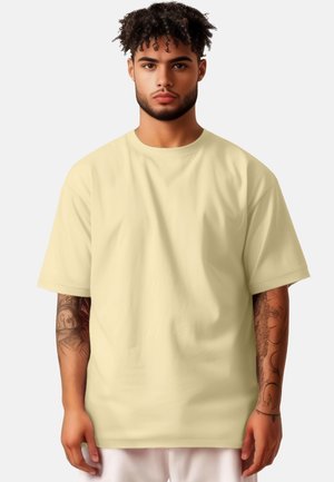 Korte mouwen t-shirt in lichtgeel, met een relaxte pasvorm en zachte textuur. Het model toont gedetailleerde arm tattoos.