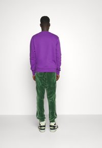 Lilla sweatshirt, grønne fløjl bukser med hvide sidelister og sort-hvide sneakers med neonlys, set bagfra.