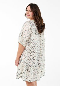 Vestido de manga corta en una tela ligera con un dobladillo en capas, que presenta un patrón de lunares en verde, marrón y azul sobre un fondo crema.