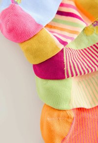 Pila de calcetines coloridos con varios patrones de rayas y talones de color sólido, dispuestos verticalmente contra un fondo claro.