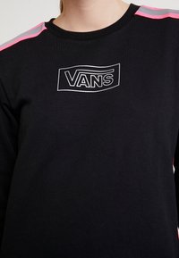 Sweat-shirt noir avec un logo Vans en blanc. De courtes rayures roses et grises ornent les épaules. Le tissu semble doux avec une coupe régulière.
