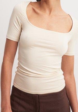 Top ajustado color crema con un amplio escote cuadrado y mangas cortas, hecho de una tela suave y elástica. Sutil fruncido en la cintura.