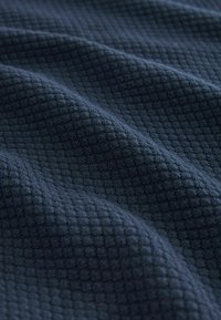 Tissu à texture gaufrée en bleu marine profond, présentant un motif en grille avec des carrés en relief, affichant des plis doux et lisses ainsi qu'un éclat subtil.