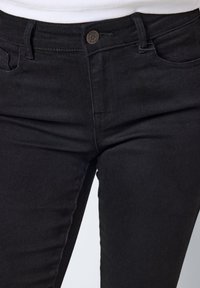 Black denim jeans with a fitted design, featuring a metal button at the waist, front pockets, and a smooth texture.