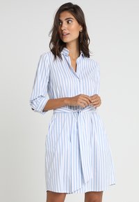 Abito camicia con colletto, a righe verticali blu e bianche, con vita a fascia e maniche a tre quarti. Tessuto in misto cotone.