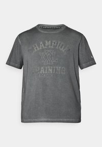 Camiseta de algodón gris con cuello redondo, que presenta un gran estampado desvaído en el frente que dice "CHAMPION XXL TRAINING ACADEMY" y un pequeño logo en la manga.