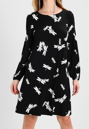 Musta mekko, jossa valkoisia sudenkorentokuvioita, pitkät puhvimaiset hihat ja pyöreä pääntie; pehmeää kangasta ja hulmuava siluetti.