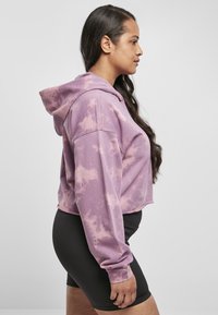 Zastihnutá mikina s kapucňou v svetlofialovej farbe s technikou tie-dye, s dlhými rukávmi a voľným strihom, kombinovaná s čiernymi šortkami s vysokým pásom.