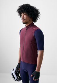 Gilet de cyclisme léger bourgogne avec un col haut, une fermeture éclair frontale et des manches courtes bleu marine. Le modèle tient un casque de cyclisme blanc.
