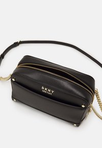 Borsa a tracolla in pelle nera con dettagli in oro, doppie cerniere e logo impresso. Presenta una tracolla in catena e tessuto con una texture liscia.