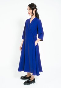 Plava haljina s dugim rukavima do tri četvrtine, lepršava tkanina i pojas. Uparena s crnim platformama za potpuni izgled.