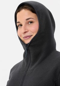 Felpa con cappuccio in grigio scuro, caratterizzata da un collo alto e chiusura con zip con accento blu. Texture morbida e vestibilità aderente attorno al viso.