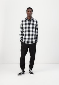 Zwart-witte geblokte shirt met een knoopsluiting, gecombineerd met zwarte joggerpants en zwarte sneakers. Schoon, casual uiterlijk.