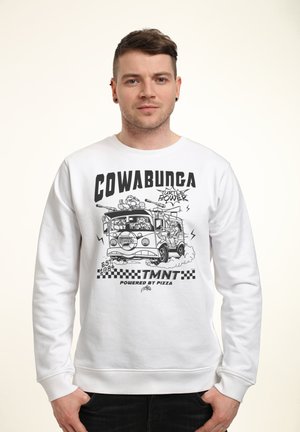 Man draagt een witte trui met zwarte afbeelding van de Teenage Mutant Ninja Turtles bestelwagen, tekst "COWABUNGA," "TMNT" en "Powered by Pizza."