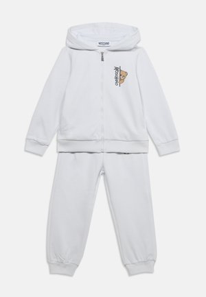 Weißer zweiteiliger Kinder-Trainingsanzug mit Reißverschluss-Kapuze, mit Teddybär und Moschino-Logo auf der Brust.