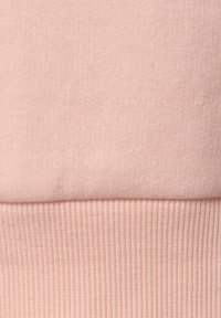 Hellrosa Sweatstoff mit glatter, gestrickter Textur und gerippten Bündchen. Die Verarbeitung zeichnet sich durch eine weiche, gleichmäßige Oberfläche aus.