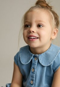 Robe en denim bleu clair avec un col, des manches courtes et des boutons en bois en forme de fleurs sur le devant. Texture lisse, design décontracté.