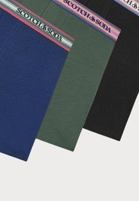Drei Paare Herrenunterwäsche in Marineblau, Grün und Schwarz. Jedes Modell hat einen bunten gestreiften Bund mit dem Logo "SCOTCH & SODA".