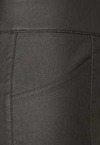 Svart, stretch denim tyg med en slät yta; har en bågformad fickdesign och kontrasterande sömmar längs kanterna.