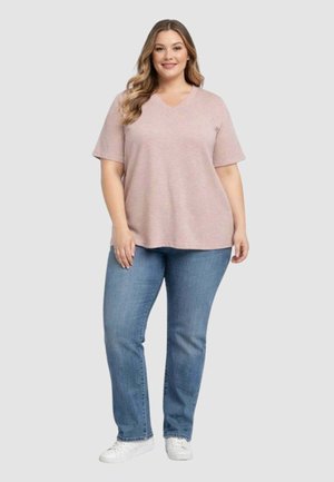 Maglietta oversize rosa chiaro con scollo a V e maniche corte abbinata a jeans a gamba dritta blu medio e scarpe da ginnastica bianche. Tessuto dalla texture liscia.