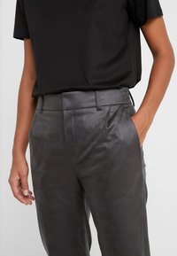 Donkergrijze neplederen broek met een gladde textuur, plooien en een op maat gemaakte pasvorm, gecombineerd met een eenvoudige zwarte t-shirt met korte mouwen.