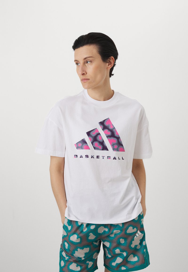 Hvid oversized t-shirt med et farverigt grafisk design, der har tre diagonale striber og teksten "BASKETBALL". Kombineret med mønstrede teal shorts.