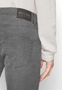 Jeans de mezclilla gris con una textura suave, que presentan un bolsillo trasero y una etiqueta de cuero negro con la marca "ONLY & SONS."