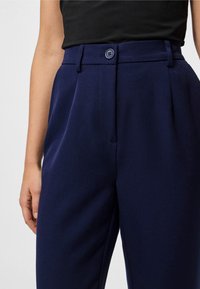 Jūras spēku zila piegriezta bikses ar platu priekšpusi, vienu pogu un sānu kabatām. Izgatavotas no strukturēta materiāla ar gludu tekstūru.