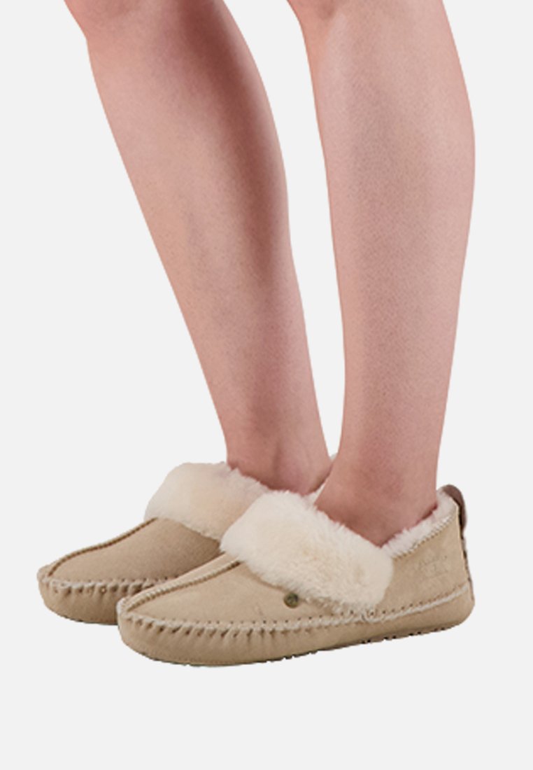 Beige pantoffels van suède, gevoerd met crèmekleurige imitatiebont. Zachte pluche manchetten en decoratieve stiksels langs de randen. Platte zolen.