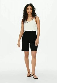 Calções pretos de corte reto e cintura alta, combinados com uma blusa branca de alças finas. Footwear apresenta tiras pretas finas.