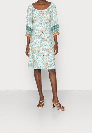 Blaues Blumenkleid mit quadratischem Ausschnitt und Puffärmeln, mit orangefarbenen Akzenten. Kombiniert mit beigen Sandalen mit Riemchen.