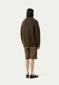Brun stickad tröja med hög krage, i kombination med bruna shorts. Tröjan har en avslappnad passform och ribbade ärmslut och nederkant.