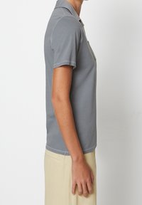 Grå polo med krage, kort ärm och slim fit. Har kontrasterande sömmar och en ficka på vänster bröst.