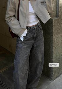Jean de gran tamaño en gris con cintura alta y piernas anchas, combinado con una chaqueta corta beige sobre una blusa blanca. Tejido suave con acentos mínimos.