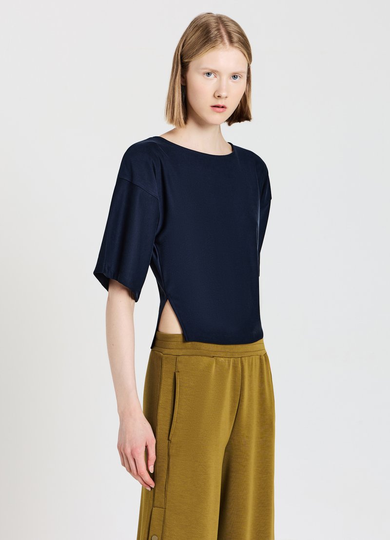 Top blu navy a maniche corte con aperture laterali, abbinato a pantaloni a gamba larga verde oliva. Entrambi i capi hanno una texture liscia e una vestibilità comoda.