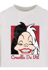 Fehér póló, amelyen egy mosolygó karakter grafikai terve látható, fekete-fehér hajjal, piros négyzet háttérrel. Felirat: "Cruella De Vil."