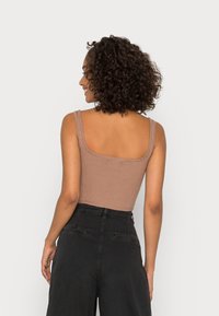 Top sin mangas de canalé marrón con tirantes anchos, diseño ajustado y escote en la espalda, combinado con pantalones negros de cintura alta con bolsillos.