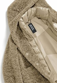 Cappotto in pelliccia sintetica marrone con un'esterno morbido e testurizzato e un rivestimento liscio di un beige chiaro. Presenta un cappuccio e una chiusura con bottoni a pressione.