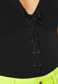 Zwarte geribbelde bodysuit met een diepe V-hals, een vetersluiting aan de voorkant met zwarte banden en metalen oogjes, gecombineerd met een fel neon groene tailleband.