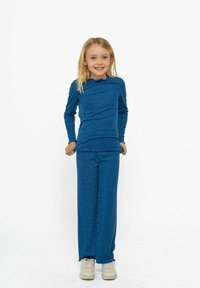 Top azul de manga larga y pantalones a juego, hechos de una tela texturizada. El top tiene un dobladillo ondulado; los pantalones son de corte relajado con una base con volantes.