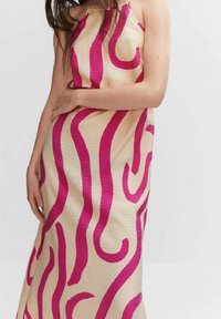 Vestido maxi en crema con llamativas rayas onduladas en rosa, con tirantes delgados y una silueta ajustada. La tela texturizada ofrece un sutil brillo.