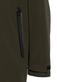 Sección de chaqueta verde oliva que presenta un bolsillo lateral con cremallera negra y ribete. El puño tiene una correa ajustable negra con un acabado texturizado.