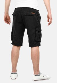 Black cargo shorts feature multiple side pockets, a relaxed fit, and a knee-length cut. Material appears durable with a slightly textured finish.