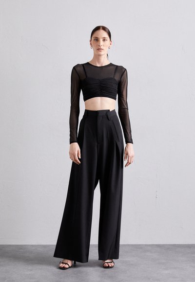 Svart cropped topp med rynket detalj og lange gjennomsiktige ermer, parret med høyhørte brede bukser i matchende svart materiale.
