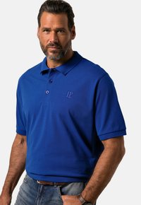 Sininen puuvillapolo-paita, jossa on kaulus, kolme nappia ja lyhyet hihat. Paidassa on huomaamaton brodeerattu logo rinnassa.