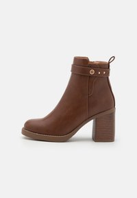 Bottine en simili cuir marron avec un bout rond, un talon large et strié, et une sangle décorative avec un accent doré et une boucle.