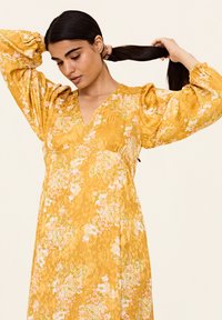 Rochie florală galbenă cu mâneci lungi bufante, decolteu în V și modele florale complicate în nuanțe de roz și verde, realizată dintr-un material ușor.