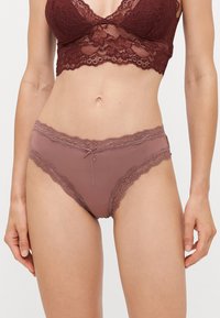 Undertøy i mauve med blondekant har et glatt materiale med bølgede kanter og en liten sløyfe i midten, som fremhever en feminin design.