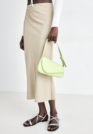 Green leather handbag with a structured shape and adjustable strap, paired with a beige midi skirt and silver strappy sandals.
