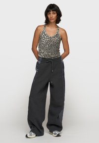 Canotta con motivo leopardato e spalline sottili, abbinata a pantaloni della tuta larghi di colore grigio scuro con pannelli in satin sui lati.